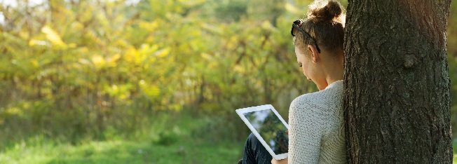 Woman using a tablet sitting under a tree